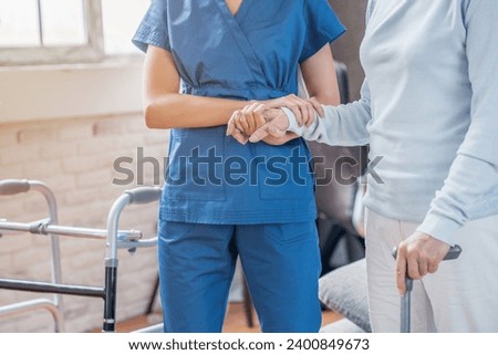 Cropped of female social worker helping senior woman to walk with walker at home. Rehabilitation after trauma injury. Active senior life. Nursing house hospice Royalty-Free Stock Photo #2400849673