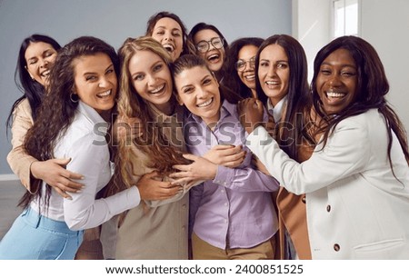 Portrait of group of happy cheerfull young diverse women friends coworkers and company employees hugging looking at camera posing and smiling on grey background. Diversity, friendship concept. Royalty-Free Stock Photo #2400851525