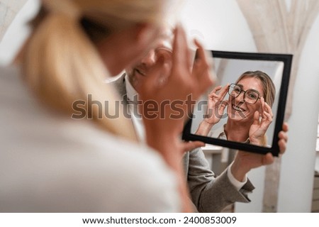 Optician holding a mirror to smiling woman trying on glasses in a optical store. Royalty-Free Stock Photo #2400853009