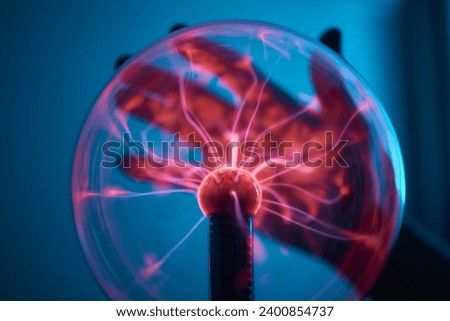 plasma ball. Hands holding plasma light ball. Plasma ball light ray science. Finger touching Plasma ball with smooth magenta blue flames. Electromagnetic Fields in a glass globe. Royalty-Free Stock Photo #2400854737