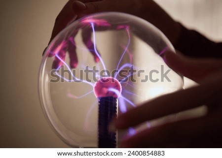 plasma ball. Hands holding plasma light ball. Plasma ball light ray science. Finger touching Plasma ball with smooth magenta blue flames. Electromagnetic Fields in a glass globe. Royalty-Free Stock Photo #2400854883