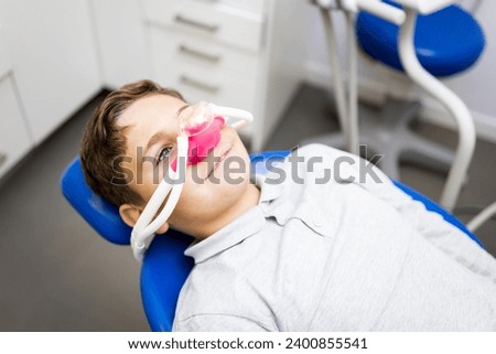 Fear of the dentist! A little boy sits in a dentist's office wearing a nasal mask to breathe nitrous oxide to relax. Concept of feeling relaxed with laughing gas. Royalty-Free Stock Photo #2400855541