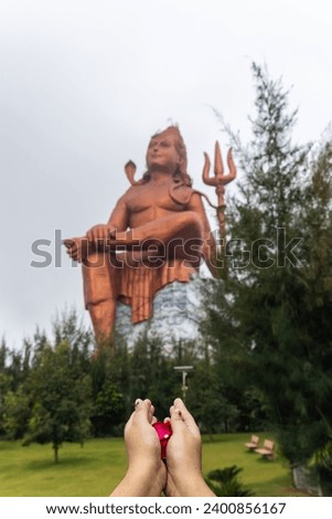 devotee praying hand with flowers and blurred hindu god lord shiva statue at morning image is taken at The Statue of Belief or Vishwas Swaroopam nathdwara rajasthan india.
