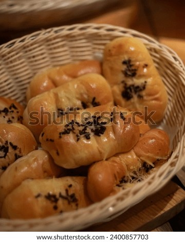 Basket of freshly baked bread rolls, golden brown, sprinkled with cheese and black seeds, plump, soft texture, savory aroma, woven basket, artisanal, homemade, comfort food, bakery, crusty exterior Royalty-Free Stock Photo #2400857703
