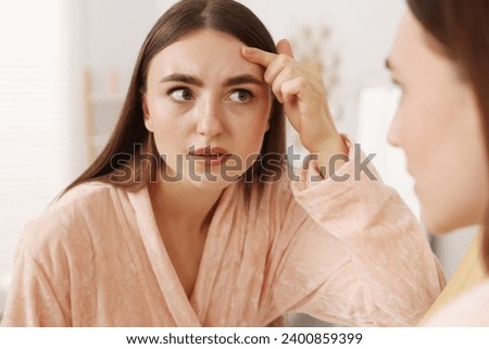 Young woman with skin problem looking at mirror indoors Royalty-Free Stock Photo #2400859399