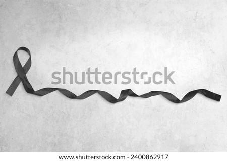 Photo of black ribbon with curled end atop a concrete background. Plenty of copy space.