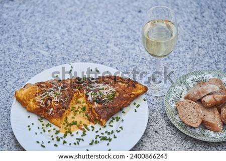 Close up picture on creamy egg omelette with sheep cheese and sprinkled by fresh green chives with slices of rustic whole grain baguette and glass of dry white wine. Quick and light dish from Bistro.