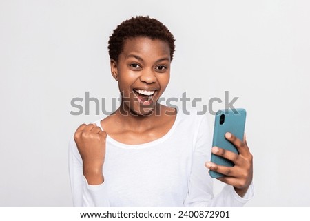 Photo of happy young African woman celebrating victory holding one fist up wearing casual white t-shirt isolated on white background in studio isolated.