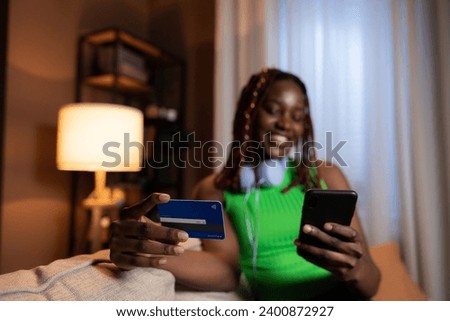 Curious delighted dreamy woman wearing casual colourful bright outfit dreaming looking up wearing new headphones holding cell phone and debir card in hands doing online purchase. Royalty-Free Stock Photo #2400872927