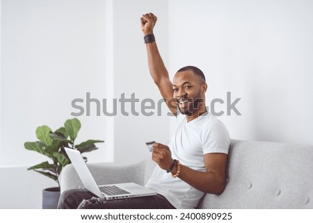 A Young happy man on laptop with credit card on couch in light livingroom