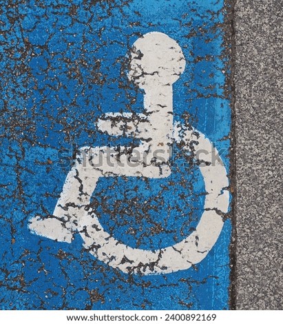Cracked white handicaped sign on blue asfalt