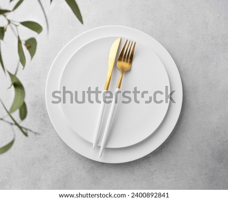 Festive table setting with empty white plate and  cutlery for holiday with eucalyptus branches on light  background. Serving concept for restaurant menu. Top view. Royalty-Free Stock Photo #2400892841