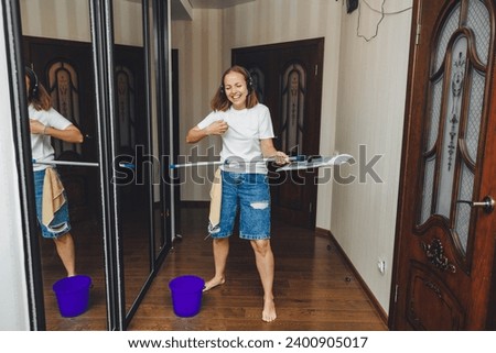 Happy young woman cleaning her house, singing with a mop like a microphone and having fun. housewife enjoying household chores, creatively cleaning the house