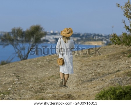 a girl in a hat and white sundress leisurely walks towards the sea Meeting the sea Alone with nature Royalty-Free Stock Photo #2400916013