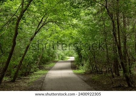 Paved path in forest near Piper Creek in summer - Red Deer, Alberta, Canada Royalty-Free Stock Photo #2400922305