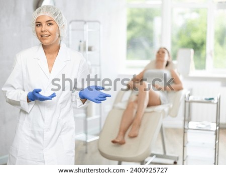 There is medical employee in disposable medical cap and gloves in office. Unrecognizable patient sitting in chair in background. Private outpatient practice. Individual approach to treatment Royalty-Free Stock Photo #2400925727