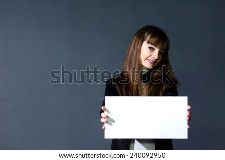 Young women holding empty white blank card on a dark wall background