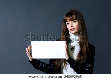 Girl with empty white blank card on a dark wall background