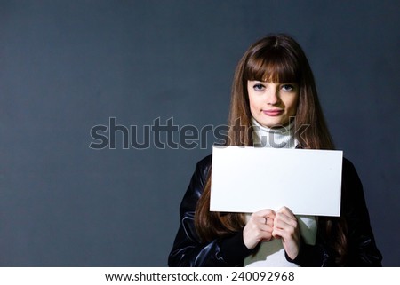 Young women holding empty white blank card on a dark wall background
