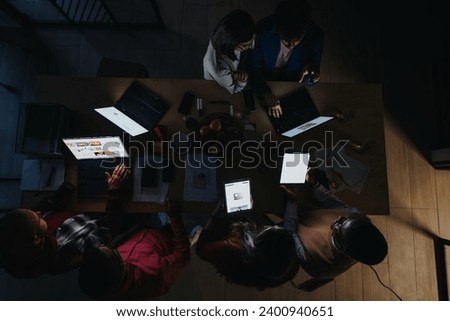 A business team analyzing statistics, discussing a marketing strategy, and working together late at night to meet project deadlines with efficiency. Royalty-Free Stock Photo #2400940651