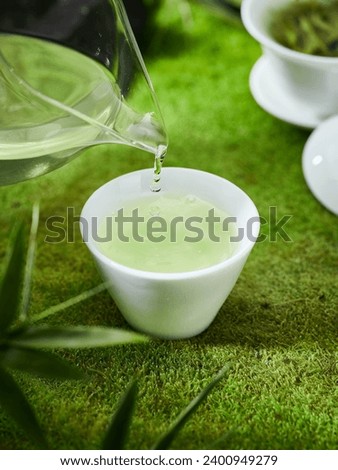 Green tea and cup on the grass, creative outdoor photography, green background, Chinese tea leaves