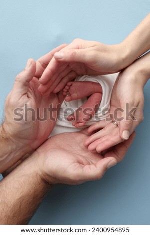 The palms of the parents, father and mother hold the legs, feet of a newborn baby in a white wrapper on a blue background. Feet, heels and toes of a newborn child close -up. Professional macro photo.