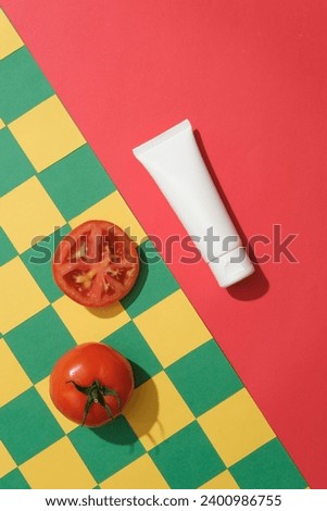 Mockup scene for advertising with creative background. A white plastic tube on red background and fresh tomatoes on green and yellow checkered background. Top view, space for design
