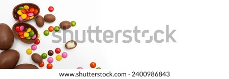 Horizontal banner. Flat lay. Chocolate eggs and multicolored small little round candies on white background. Copyspace for text. Concept of Happy Easter holiday, healthy food, sweets, gift, egg hunt