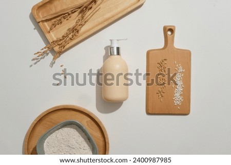 Rice bran powder is stored in a ceramic bowl. Wooden trays with different shapes and a bottle of shower gel on a white background. Natural extracts in cosmetics.