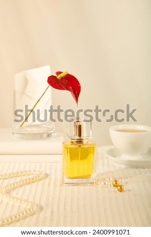 Front view of a yellow perfume bottle displayed on beige background with vase of red flower, cup of coffee and pearl necklace. Scene for advertising essential oil product with mockup for design