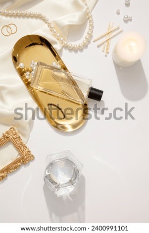 Fashion composition with accessories on white background. Pearl necklace, ring, scented candle and fabric decorated. A glass perfume bottle unlabeled displayed on gold tray. Mockup for design