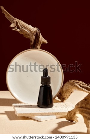 A black dropper bottle placed on brick podiums decorated with dry twigs and round dish on brown background. Front view, creative concept for advertising with minimal style Royalty-Free Stock Photo #2400991135