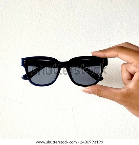 A hand holding sunglasses in front of a white background