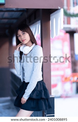 young asian girl wearing warm clothes with wearing white wireless headphones and listening to music in the park outdoors or at the cafe in background Decoration During Christmas and New Year Festival