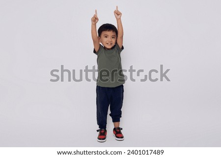 Full body little small smiling happy Asian boy 2-3 years old wearing green t-shirt standing confident while doing winner gesture isolated on white background Royalty-Free Stock Photo #2401017489