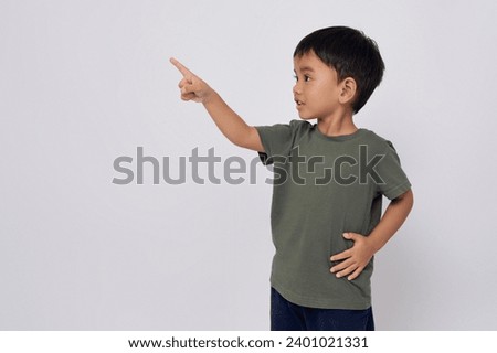 Smiling happy Asian boy 2-3 years old wearing a green t-shirt pointing finger at copy space isolated on white background Royalty-Free Stock Photo #2401021331