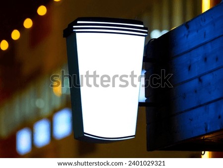 Cup sign mockup and blank frame template for logo, brand, advertising on blue wall background.  Wall mounted outdoor presentation sign with night lighting.