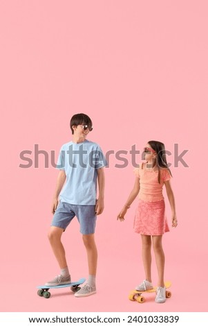 Cute girl and her brother with skateboards on pink background