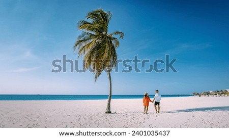Eagle Beach Aruba, Palm Trees on the shoreline of Eagle Beach in Aruba, couple man, and woman on the beach of Aruba walking on the beach in the evening during vacation Royalty-Free Stock Photo #2401035437
