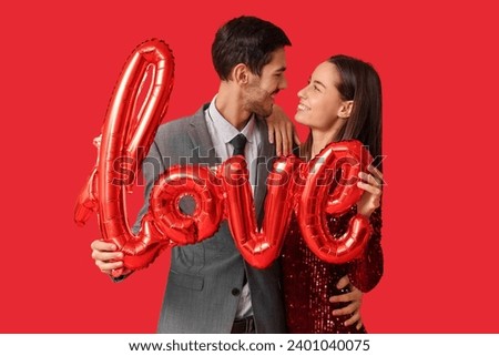Beautiful young couple with air balloons in shape of word LOVE on red background. Valentine's day celebration
