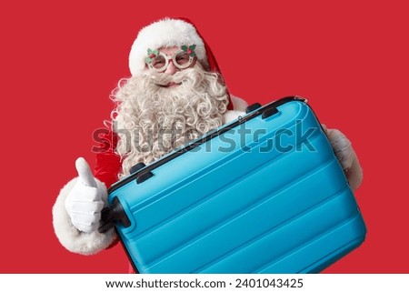Santa Claus with suitcase showing thumb-up gesture on red background. Christmas vacation concept