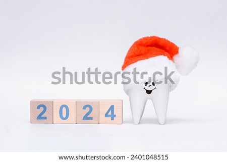 smiling healthy tooth in a Santa Claus or Father Frost hat on a white background with the numbers of the year 2024. Christmas or New Year gift for the dentist