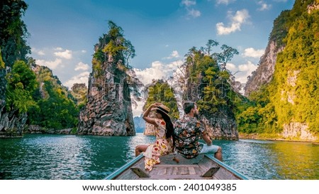 a couple traveling by longtail boat exploring epic limestone cliffs in a huge lake in Khao Sok National Park, Chiew Lan Lake, Thailand Surat Thani, men and woman in front of longtail boat Royalty-Free Stock Photo #2401049385