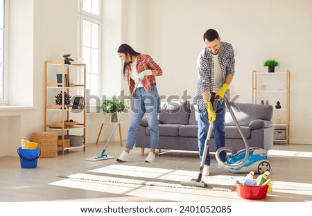 Young happy couple engages in home cleaning, with a vacuum and mop. They demonstrate togetherness and joyous teamwork, transforming household chores into moments of family connection.