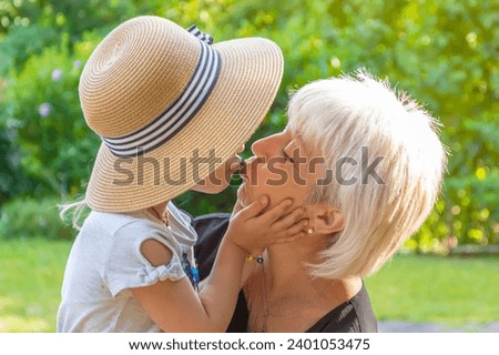 A little granddaughter hugs her elderly grandmother lovingly against the backdrop of nature.