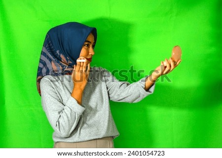 beautiful Asian muslim woman in grey cloth hijab woman doing a make up isolated over green background. People religious lifestyle concept.