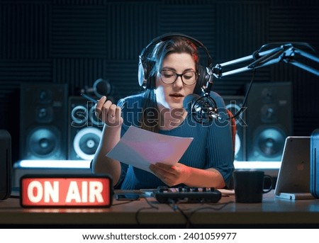 Female radio host working in the radio studio, she is holding sheets and talking into the microphone
