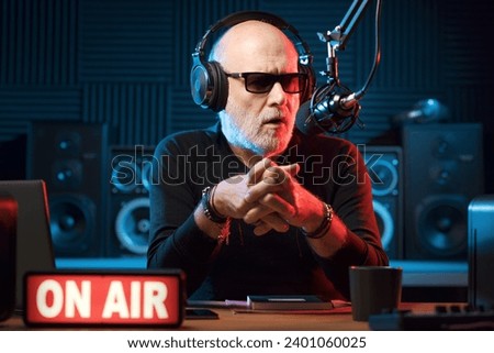 Professional expressive radio presenter working at the radio station, he is wearing headphones and talking into the microphone