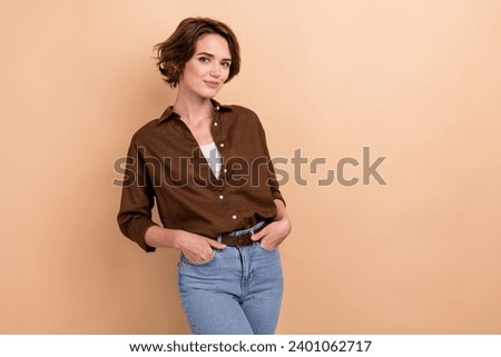Photo of lovely nice woman with bob hairstyle dressed brown shirt holding arms in pockets posing isolated on beige color background