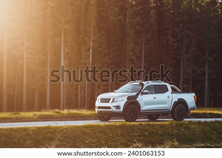 A pickup truck with a snorkel drives on a scenic road surrounded by mountains and trees. Royalty-Free Stock Photo #2401063153